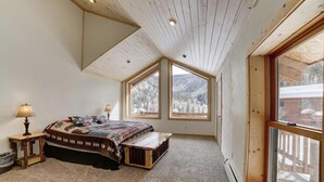 Un dormitorio con una cama grande, paredes de madera y múltiples ventanas que ofrecen vistas a un paisaje nevado.