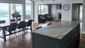 Une cuisine spacieuse dotée d’un grand îlot central, de planchers en bois foncé et offrant une vue sur l’extérieur grâce à de grandes fenêtres.