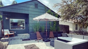 A patio area with outdoor furniture, a striped umbrella, and a view of a house with the number 371. - BEST location in Bend! ~HOT TUB!~ (Bend)