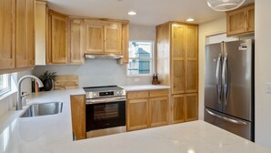 A modern kitchen with wooden cabinets, stainless steel appliances, and pendant lighting. - BEST location in Bend! ~HOT TUB!~ (Bend)