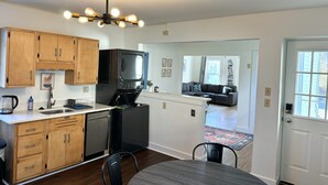 A compact kitchen with wooden cabinets, a black refrigerator, a built-in oven, and a dining area with a table and chairs.