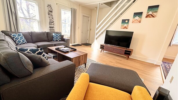 A modern living room with a sectional sofa, a yellow armchair, a coffee table, and a flat-screen TV.