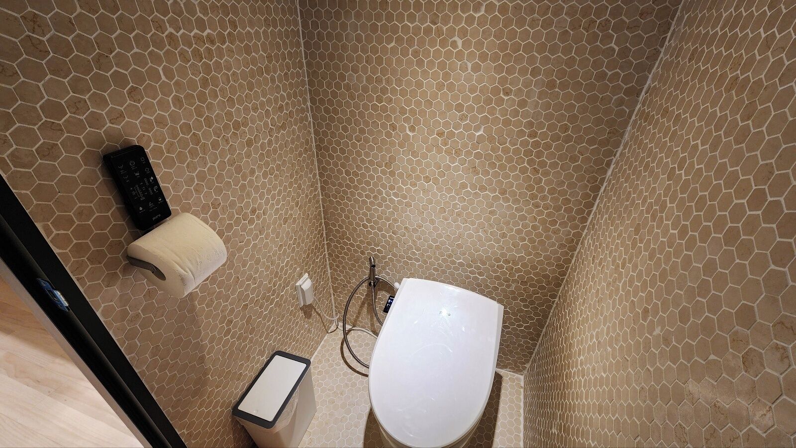Une salle de bain avec un carrelage à motifs hexagonaux, des toilettes, un distributeur d’essuie-tout et un sèche-mains.