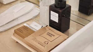 A bathroom counter with a hand care product, bamboo toothbrush, and a shower towel.
