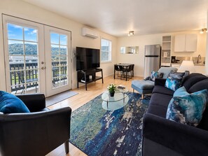 Een moderne woonkamer met een bank, een salontafel en een televisie. Er is een balkon met uitzicht op het landschap.