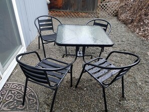 Un espace patio avec une table en métal et quatre chaises, entouré de gravier.