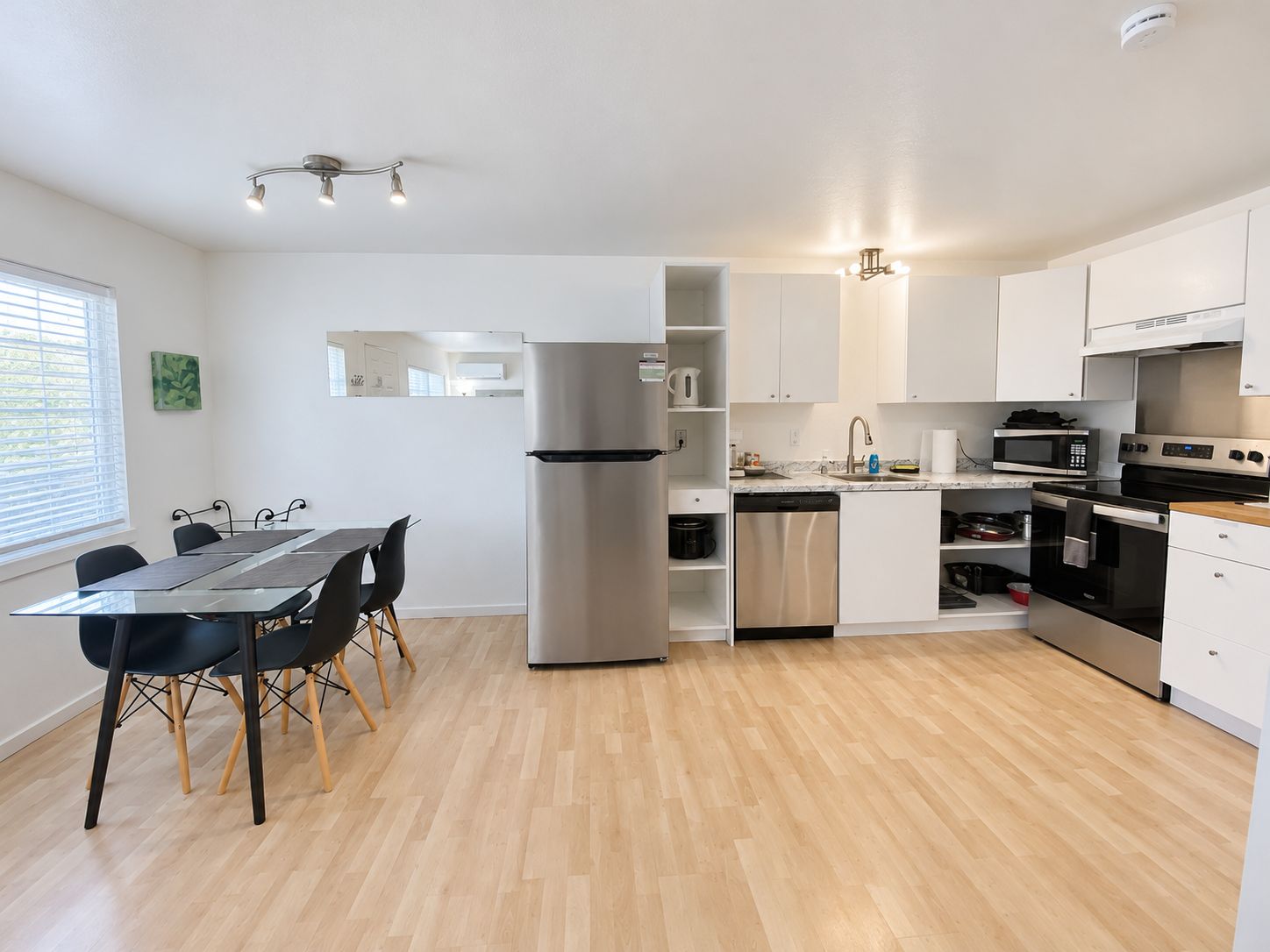 A modern kitchen with a dining area, stainless steel appliances, and a wooden floor.