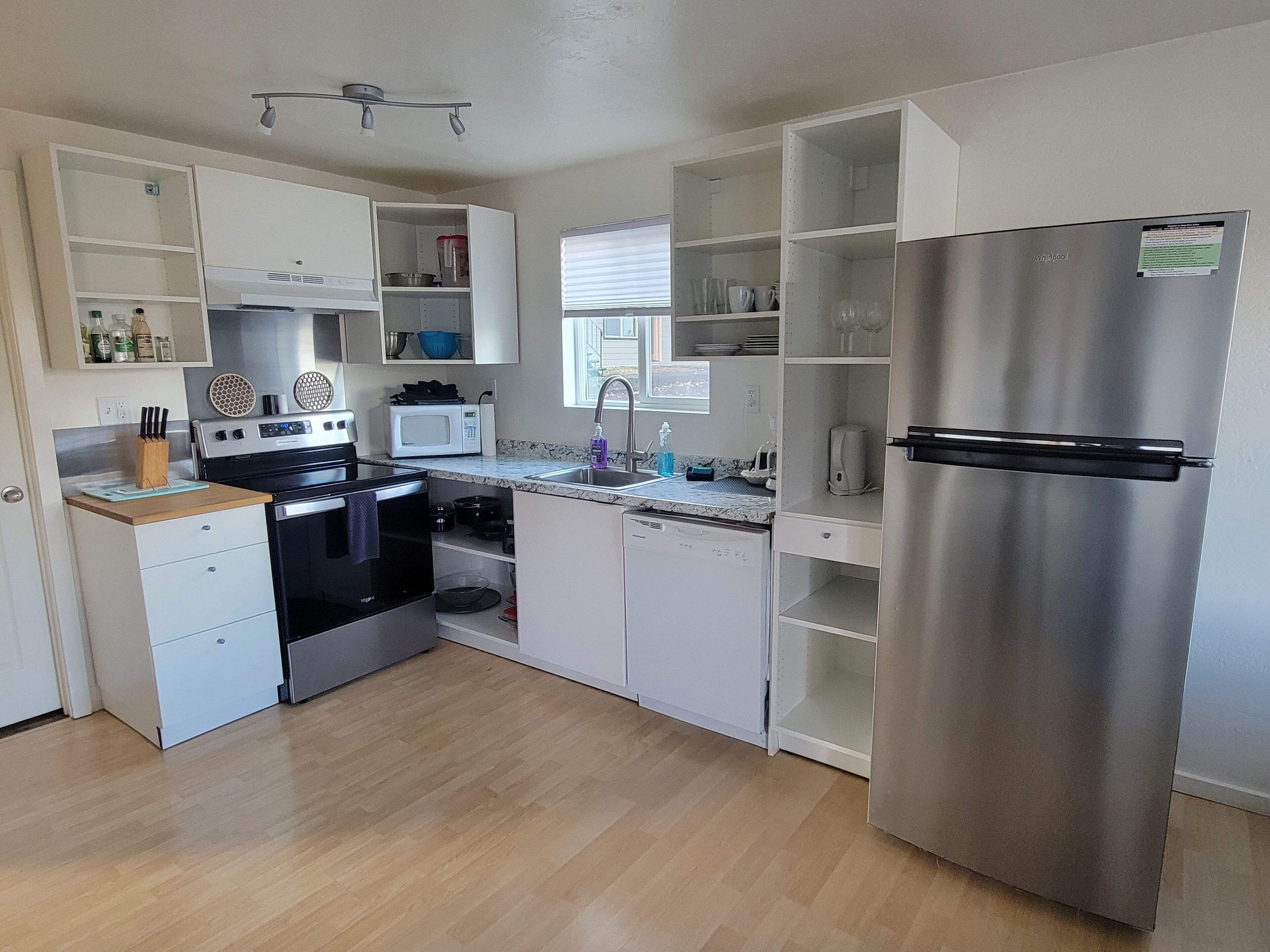 A modern kitchen with stainless steel appliances, white cabinetry, and a wooden countertop.