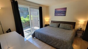 A bedroom with a bed, a desk, a chair, a nightstand, and a window with curtains.