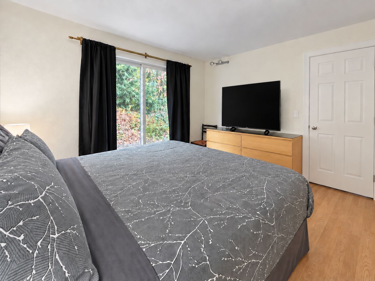 A bedroom with a large bed, a dresser, a television, and a door.
