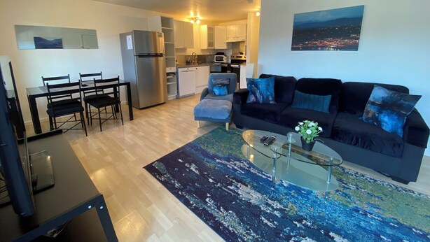 A modern living room with a black sofa, a glass coffee table, and a dining area with a black table and chairs.