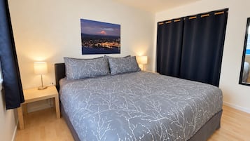 Un dormitorio con cama, dos mesitas de noche, una lámpara de noche, ventana con cortinas y un cuadro colgado en la pared.