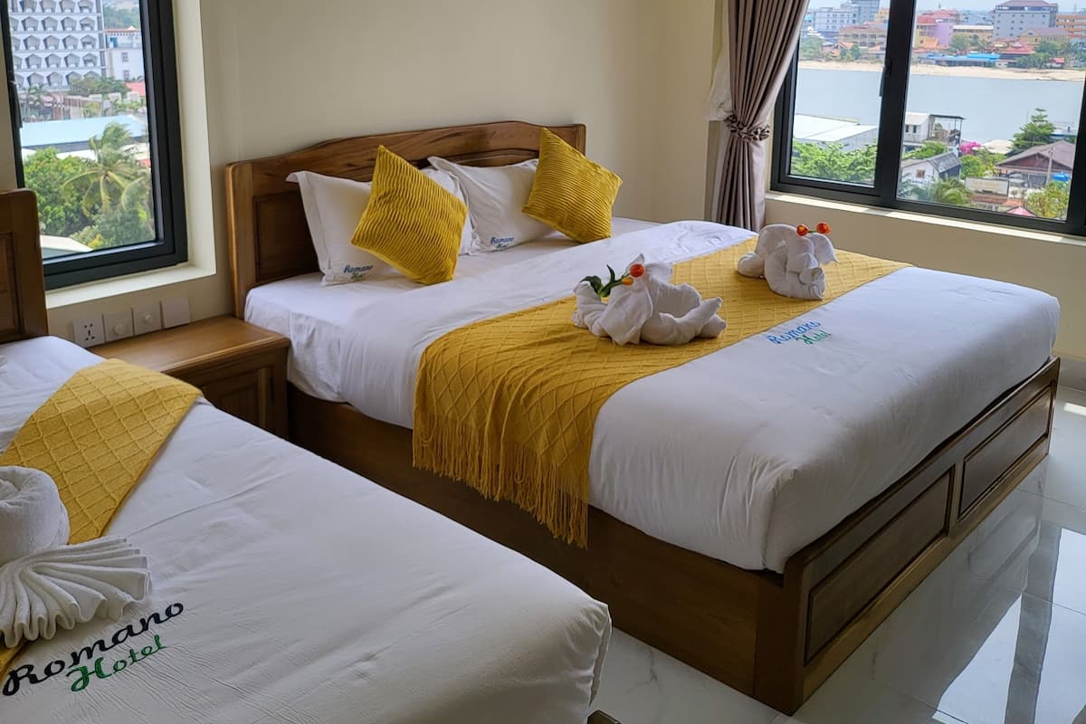 A hotel room with two beds, a large window with a view of a body of water and buildings, and artwork on the wall.