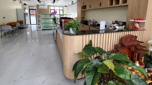 A modern reception area with a wooden counter, a refrigerator, and a seating area with tables and chairs. - Romano Hotel (Kampot)