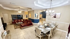 A spacious living area with a red leather sofa, a dining table set for four, and a kitchen in the background. - Hidden Treasure-cozy and stylish 3BR with salt water heated pool (Palm Coast)