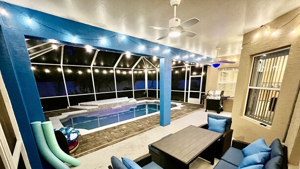A pool area with a blue wall, seating, and a ceiling fan. - Hidden Treasure-cozy and stylish 3BR with salt water heated pool (Palm Coast)