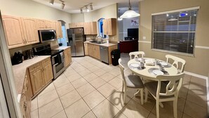 A modern kitchen with wooden cabinets, stainless steel appliances, and a dining area with white chairs and a table. - Hidden Treasure-cozy and stylish 3BR with salt water heated pool (Palm Coast)