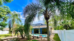 A backyard with a pool, a house with a blue exterior, and various trees. - Hidden Treasure-cozy and stylish 3BR with salt water heated pool (Palm Coast)
