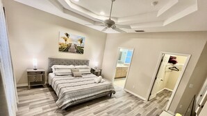 A bedroom with a bed, nightstands, a ceiling fan, and a painting on the wall. - Hidden Treasure-cozy and stylish 3BR with salt water heated pool (Palm Coast)