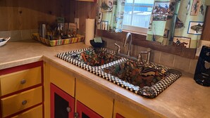 Une cuisine avec un évier carrelé à motifs, des placards en bois et une fenêtre ornée de rideaux à motifs.