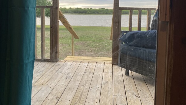 Une terrasse en bois offrant une vue sur un lac, une chaise bleue et une rambarde en bois.