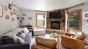 A living room with a stone fireplace, a sofa, a leather armchair, and a coffee table. - Welcome to the Middle Fork Cabin of Fairplay (Fairplay)