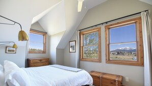 A bedroom with a bed, a wooden bench, two windows with mountain views, and a ceiling fan. - Welcome to the Middle Fork Cabin of Fairplay (Fairplay)