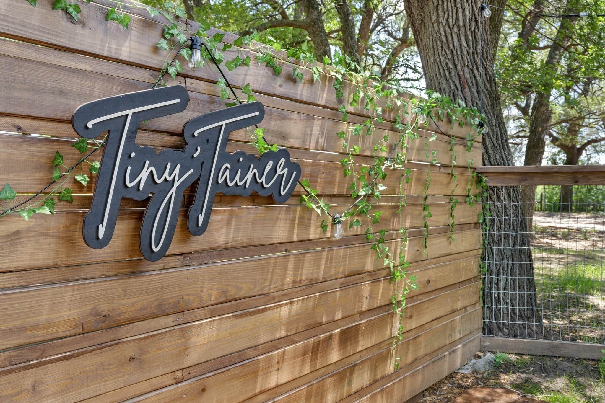 A wooden wall with the name "Tiny Tainer" in stylized lettering.