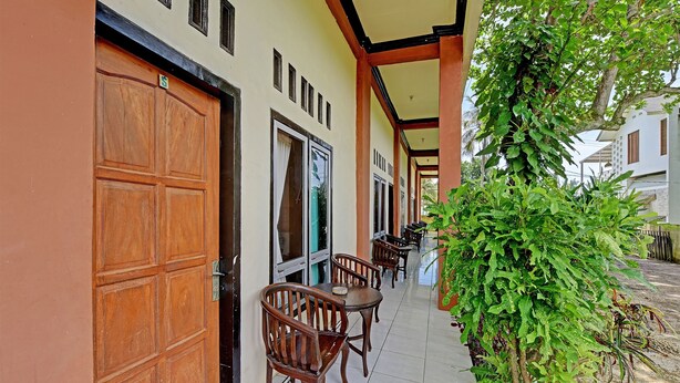 A corridor with wooden doors and windows, a tiled floor, and a potted plant. - OYO 91877 Mushroom Pondok Ator Syariah Hotel (Pangandaran)