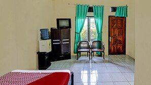 A hotel room with a bed, a television on a cabinet, a water dispenser, and a wooden door. - OYO 91877 Mushroom Pondok Ator Syariah Hotel (Pangandaran)