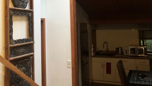 Eine Holztreppe mit dekorativer Metallreling, einem Oberlicht sowie einer Küchenzeile mit Spüle, Mikrowelle und Schränken.