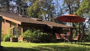 Eine Holzhütte mit überdachter Terrasse, Sitzgelegenheiten im Freien und einem großen Sonnenschirm.