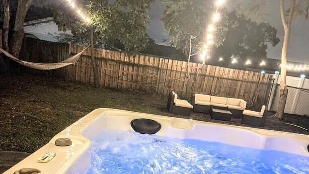 Un bain à remous entouré d’une clôture en bois, avec des guirlandes lumineuses en arrière-plan.