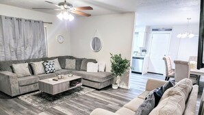 Un salon moderne avec un canapé d’angle, une table basse et un coin repas comprenant une chaise.