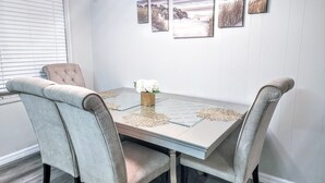 Un coin repas avec une table dressée pour quatre personnes, agrémenté de chaises capitonnées et d’un vase de fleurs.