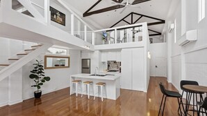 Een ruim appartement in loftstijl, met een centrale keuken, een eethoek en een trap naar een hoger niveau.
