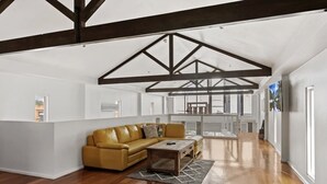 Een ruime loft met hoge plafonds, zichtbare houten balken, een groot raam en een gele leren bank.