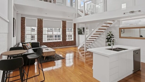 Een ruim loft appartement met een ruime open leefruimte, een keuken met een wit kookeiland, een trap en uitzicht op de stad.