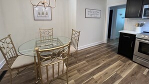 A modern kitchen with a dining area, featuring a glass-top table, metal chairs, a chandelier, and a kitchen island with a built-in oven. - Restful Mid-Mod in the heart of Hickory (Hickory)