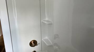 A modern bathroom with a bathtub, a shower, and a toilet. There are three shelves for toiletries.