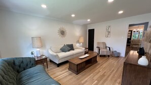 A spacious living room with a large sectional sofa, a smaller sofa, a coffee table, and a chair. The room has wooden flooring and recessed ceiling lights. - Restful Mid-Mod in the heart of Hickory (Hickory)