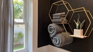 A bathroom with a window, a towel rack with towels, and a geometric shelf with a plant. - Restful Mid-Mod in the heart of Hickory (Hickory)