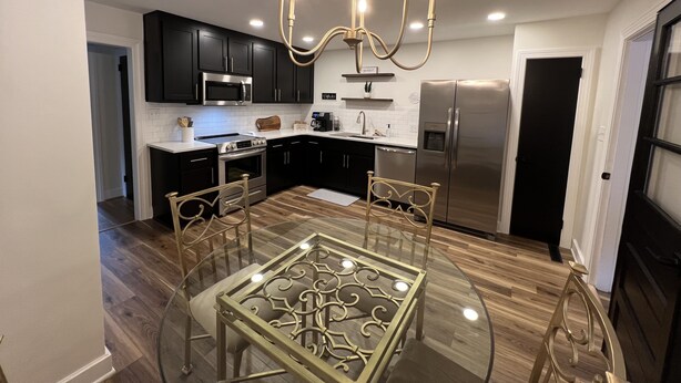 A modern kitchen with black cabinets, stainless steel appliances, and a glass dining table with chairs. - Restful Mid-Mod in the heart of Hickory (Hickory)