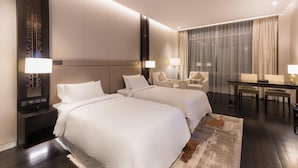 Een hotelkamer met twee bedden, een bureau, stoelen en een groot raam met gordijnen.