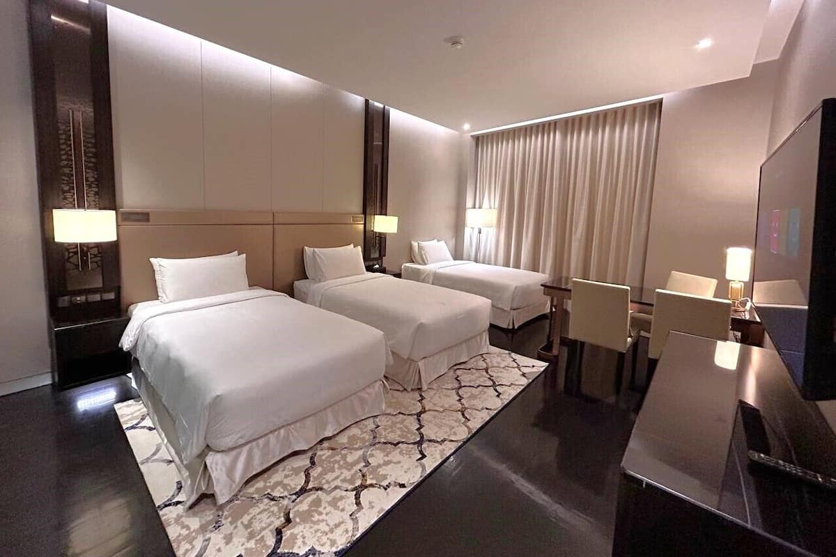 Habitación de hotel con dos camas, un escritorio, una silla, un televisor y una ventana con cortinas.