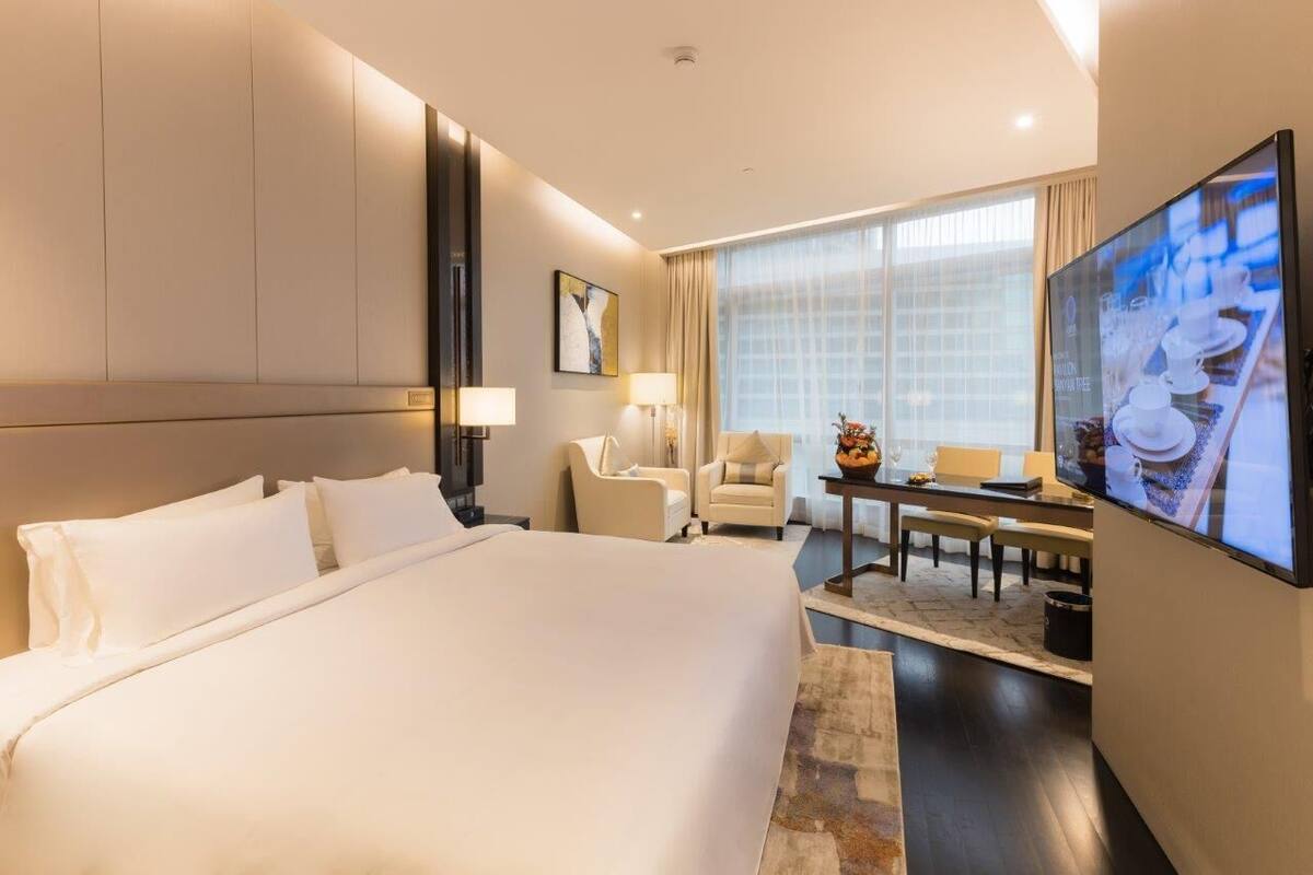 Habitación de hotel con una cama grande, un escritorio, dos sillas, un televisor y una ventana con cortinas.