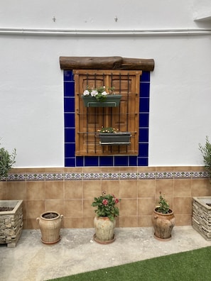 Una pared con un marco de ventana de madera, dos jardineras colgantes y tres macetas en el suelo.