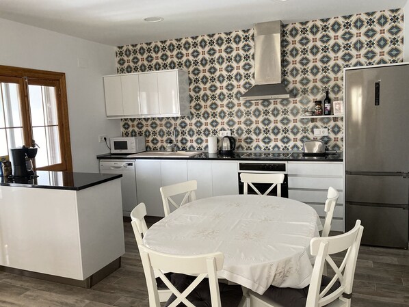 A modern kitchen with white cabinetry, a central island with a dining table, and a patterned backsplash.