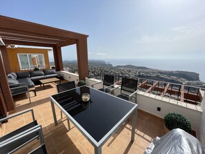 A terrace with a sofa, chairs, and a table, overlooking a coastal town and cliffs. - Apartamento con Terraza y Vistas Unicas (Benitachell)