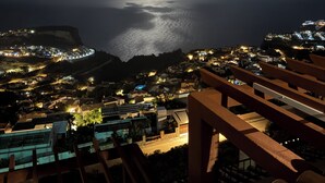 Une vue nocturne de la côte, avec une lune bien visible, une plage et une ville dont les bâtiments sont illuminés.